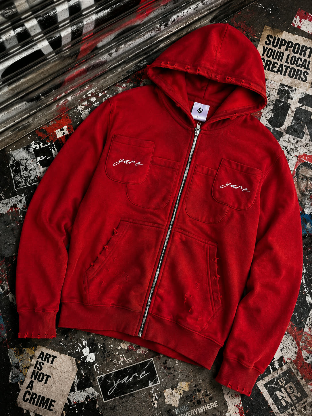 Double Pocket YARE Jacket in bright red laid flat on a black and red street-art surface
